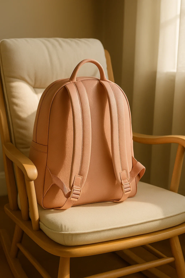 a clear backside of the a pinkish diaper leather backpack sits on a chair